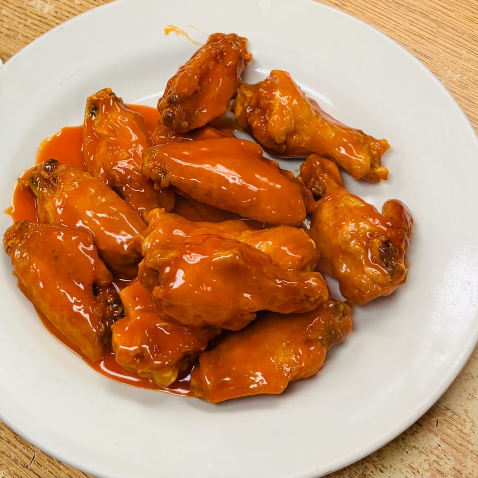 Plate of crispy chicken wings coated in glossy orange sauce on a white dish atop a wooden table.