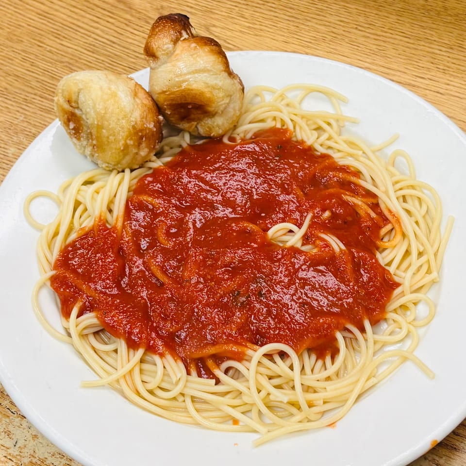 Plate of spaghetti topped with tomato sauce and served with three golden garlic knots on a wooden table.